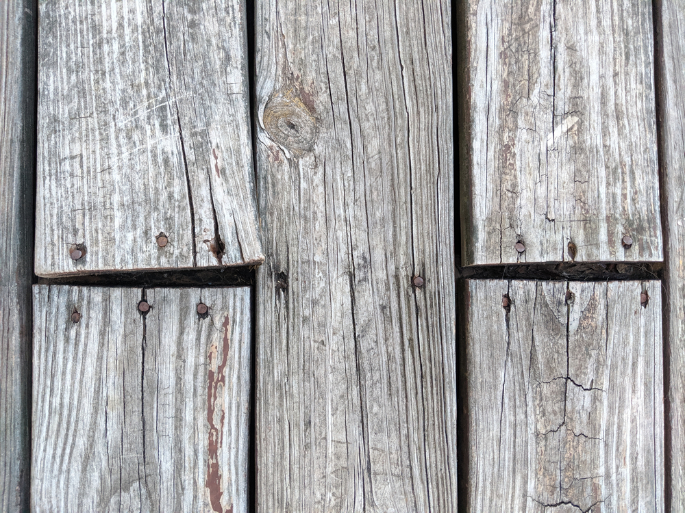 Top view of wooden deck floor boards coming up, warped and weathered, needing to be nailed and repaired